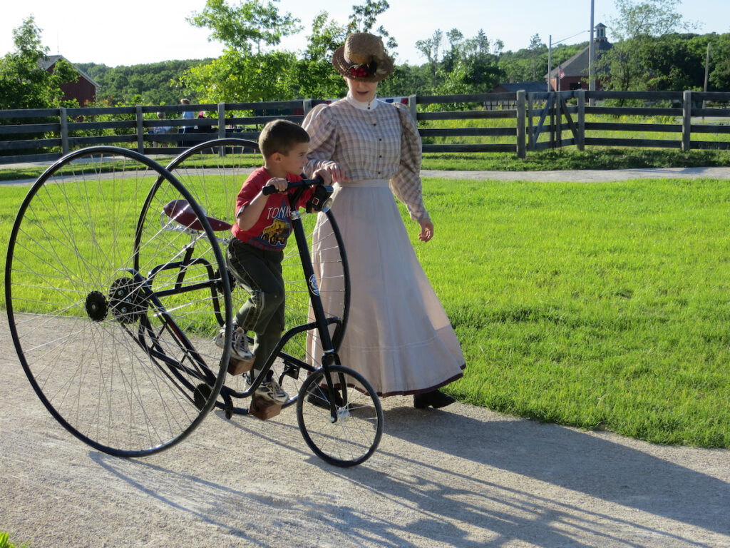 A woman in period costume helps guide a young boy on a vintage bicycle, as part of her employment at Old World Wisconsin. 
