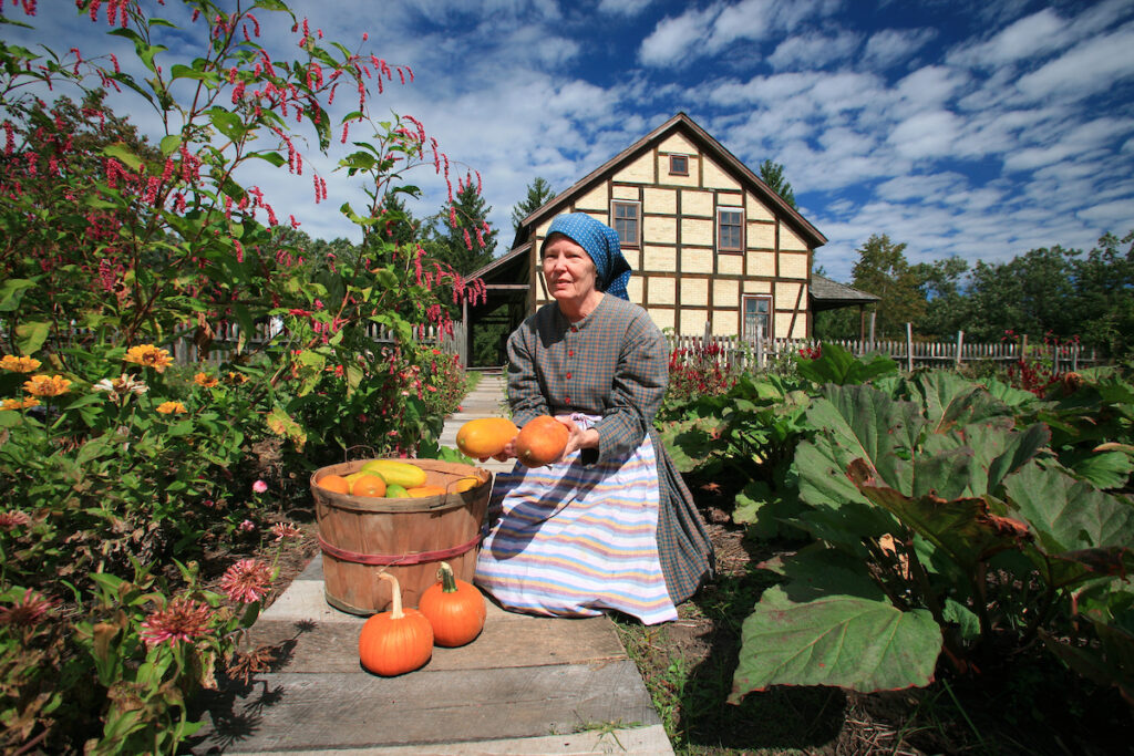 A woman holding two squash near a basket full of squash in period costume during her employment at Old World Wisconsin.