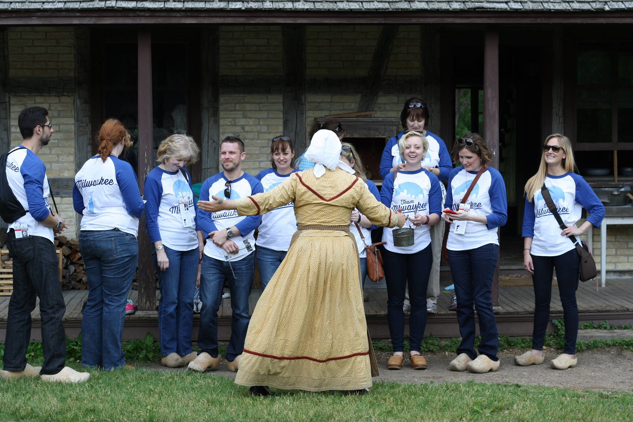 A woman from period time clothing talking to a group of people wearing blue team Milwaukee shirts on a tour