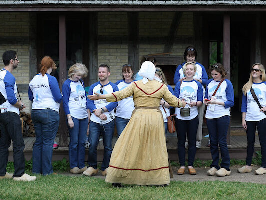 a group of people people wearing blue team Milwaukee shirts on a tour in front of a woman dressed in period time clothing