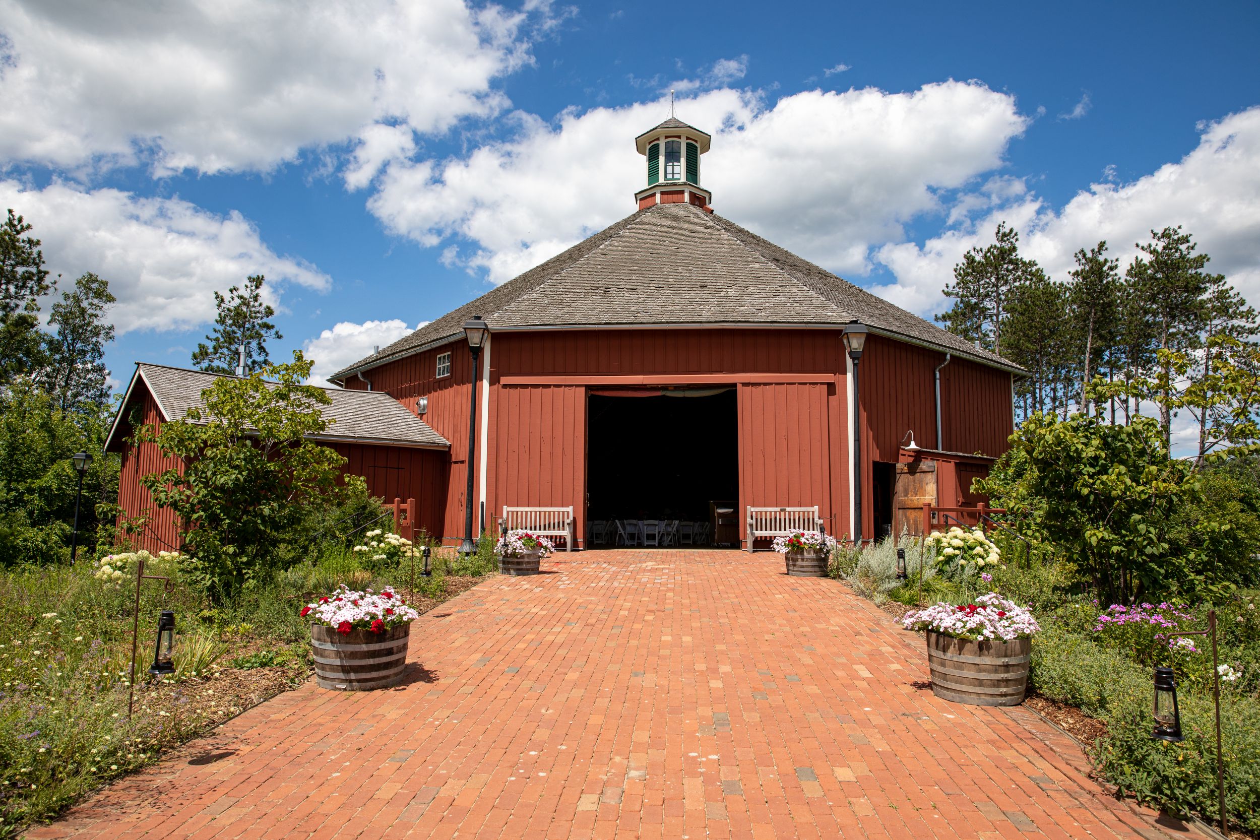 A red barn with the door open and greenery and flowers around it