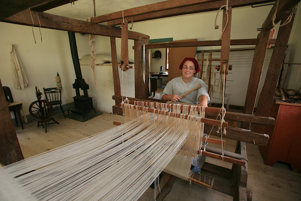 Someone dressed in period time clothing weaving on a loom
